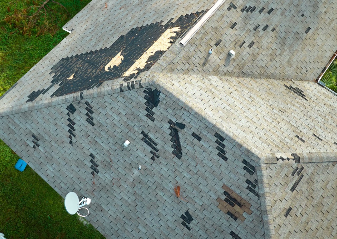 Storm damaged residential roof with missing shingles and exposed decking